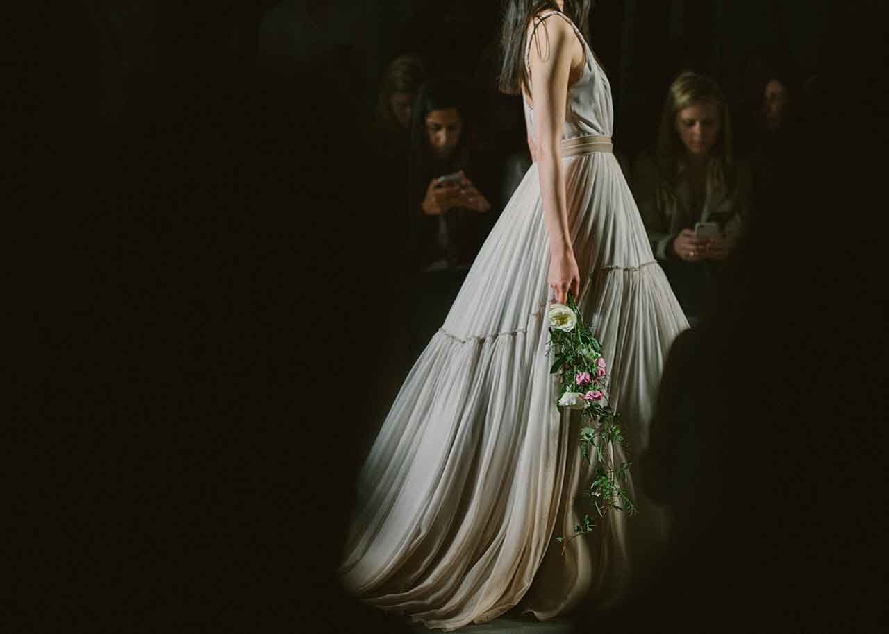 mike colon shot of female model in wedding dress, holding bouquet, walking on fashion runway