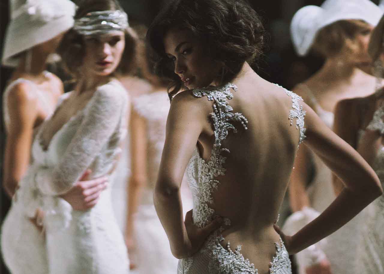 mike colon shot of female model wearing backless lace wedding dress surrounded by other models